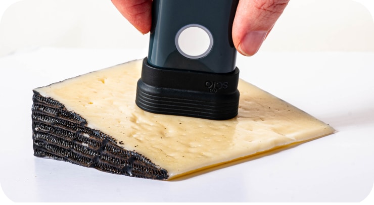 A device is being pressed onto a wedge of cheese with a black rind.