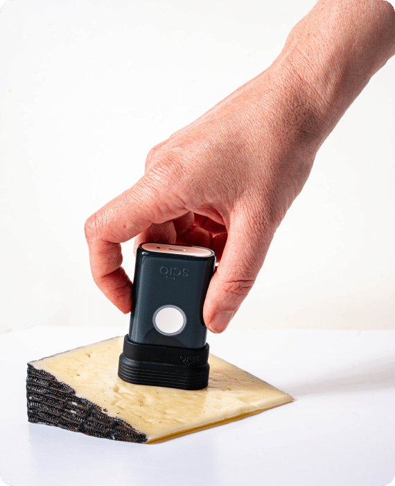 A person presses a handheld scanner against a wedge of cheese on a flat surface.
