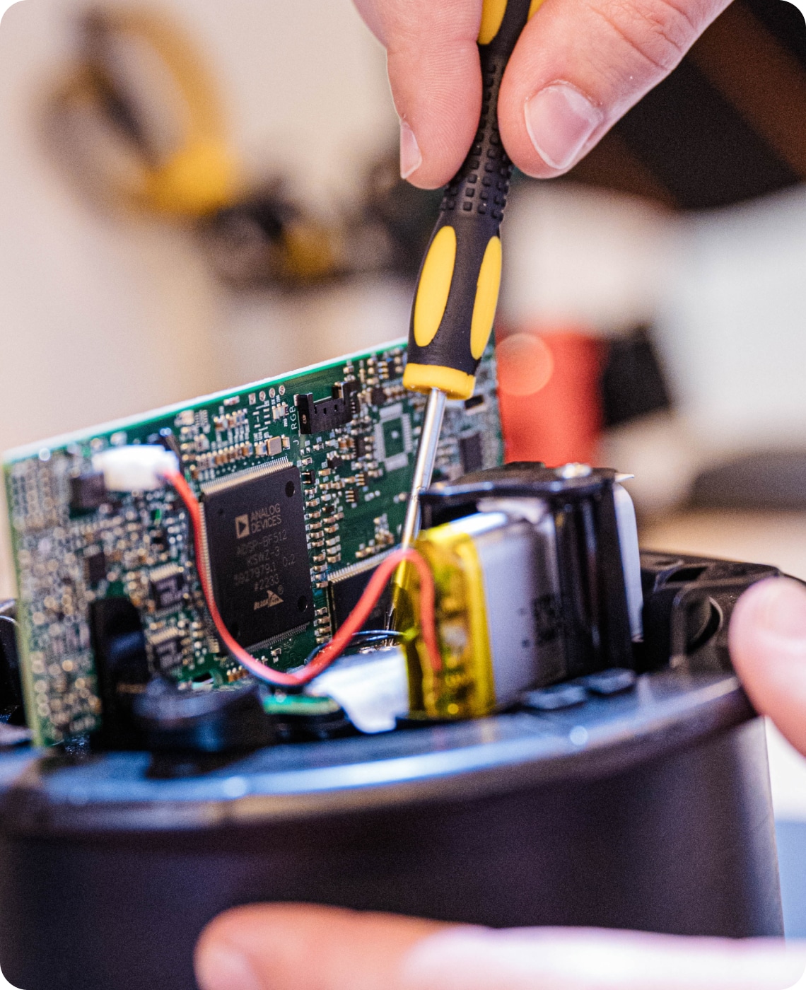 A person uses a screwdriver to work on an open electronic device revealing a circuit board and wires.
